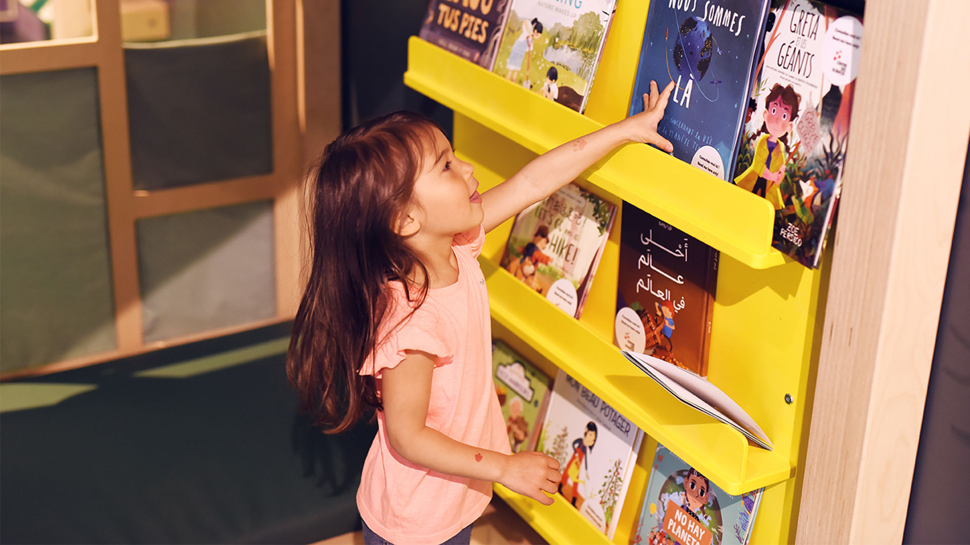 A young child reaches to a book on a bookshelf