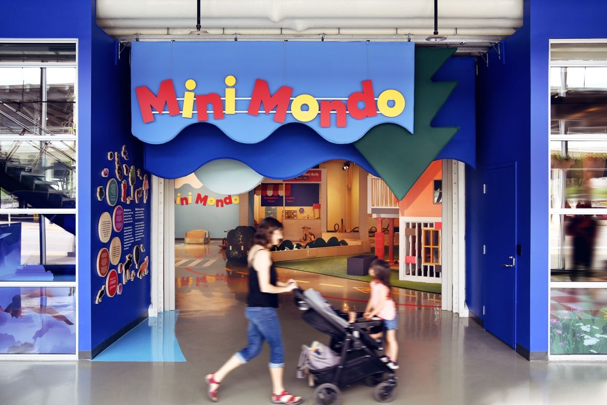 A woman pushes a child in a stroller past the entrance to the Mini Mondo exhibition