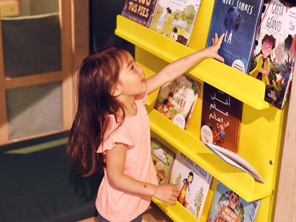 A young child reaches to a book on a bookshelf