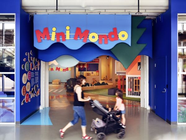 A woman pushes a child in a stroller past the entrance to the Mini Mondo exhibition